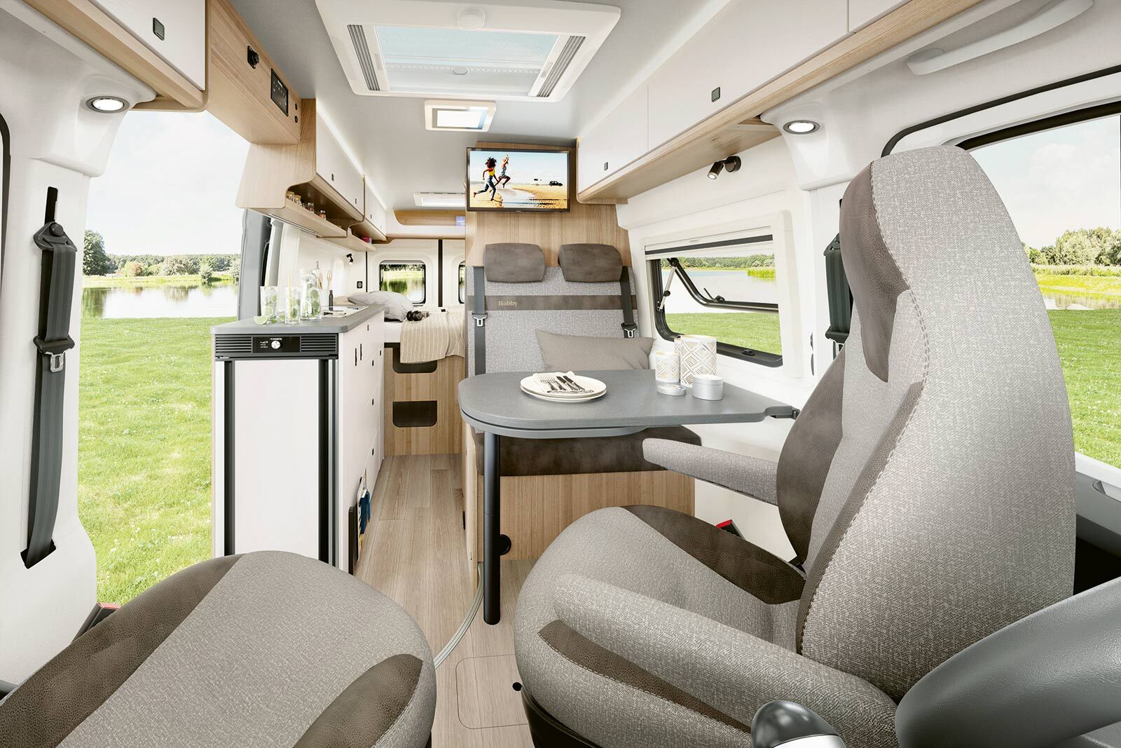 L’aménagement clair et moderne comprend une dînette confortable avec sièges de cabine pivotants, un bloc cuisine compact avec réfrigérateur et un lit arrière fixe en arrière-plan.